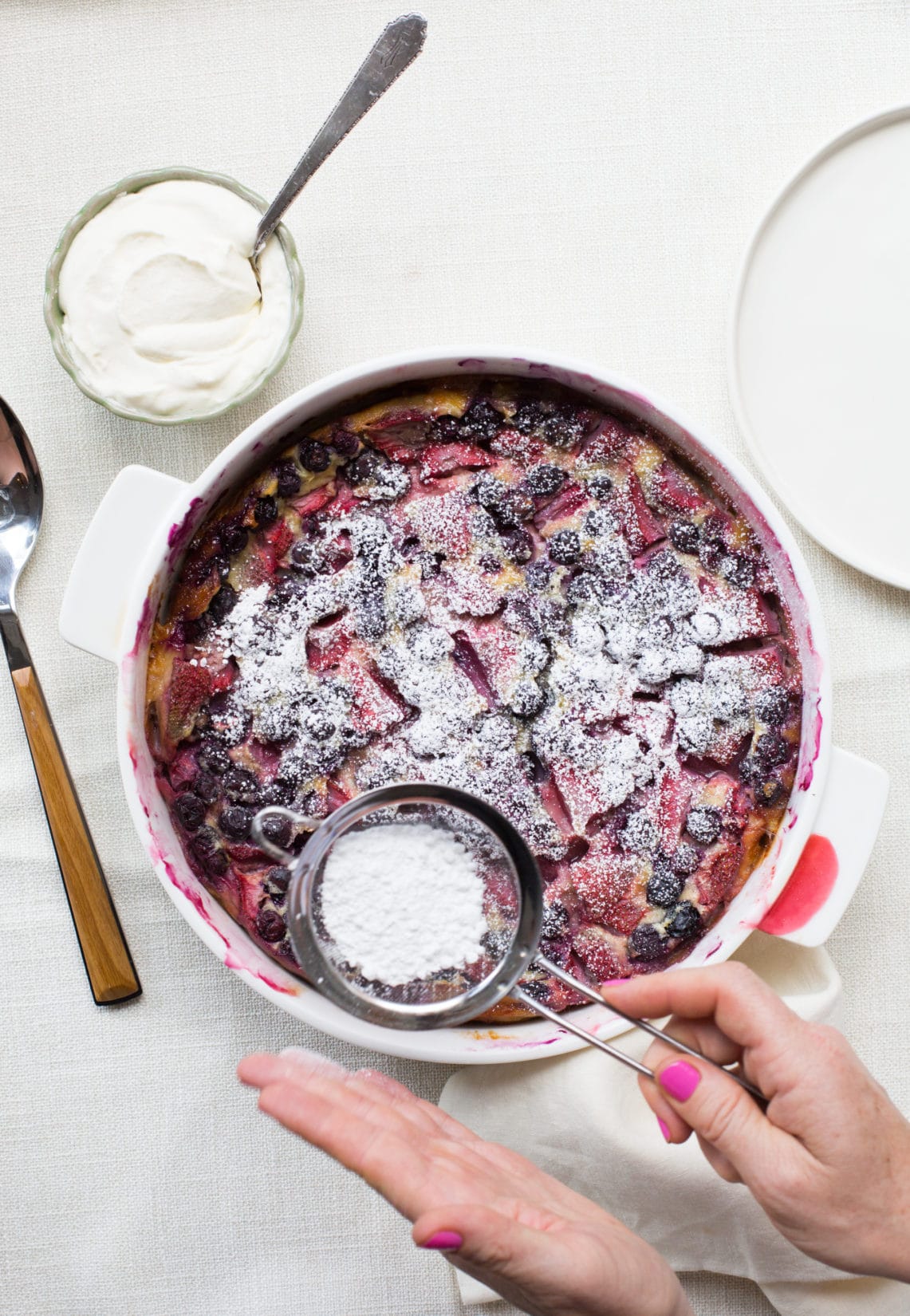 Woman sprinkling powdered sugar onto a dish of Summer Berry Clafoutis.