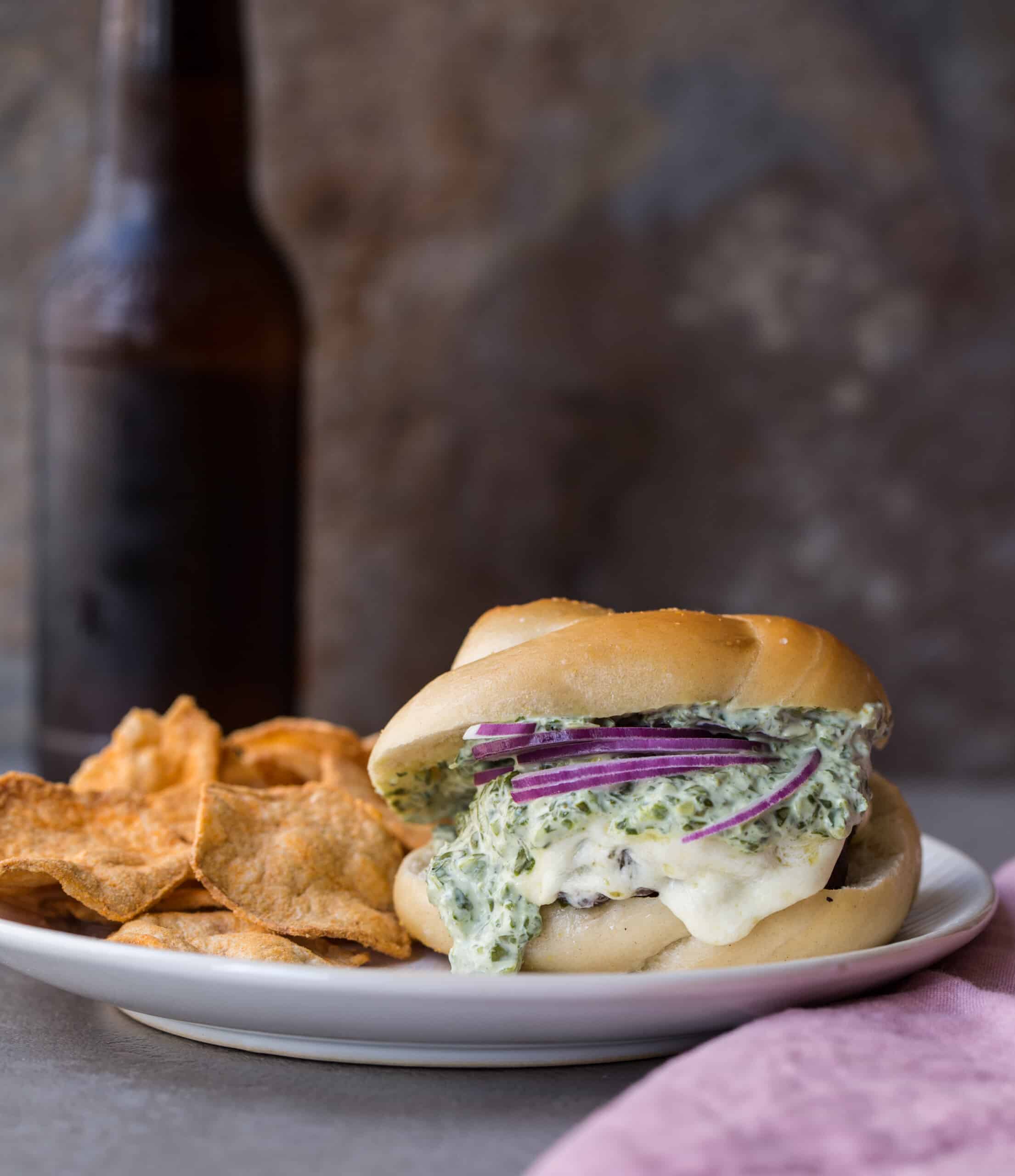 Grilled cheeseburger with herb sauce on a plate with chips.