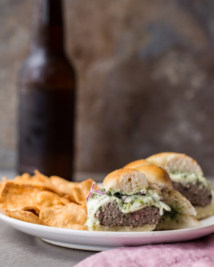 Chips and a halved Grilled Cheeseburger with Herb Sauce missing a bite on a plate.