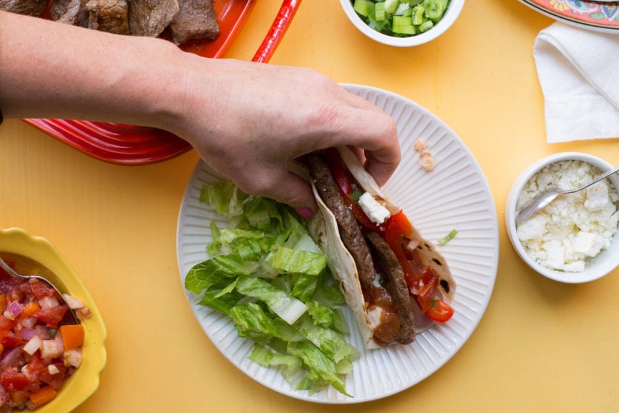 Woman grabbing a Steak Fajita from a plate.