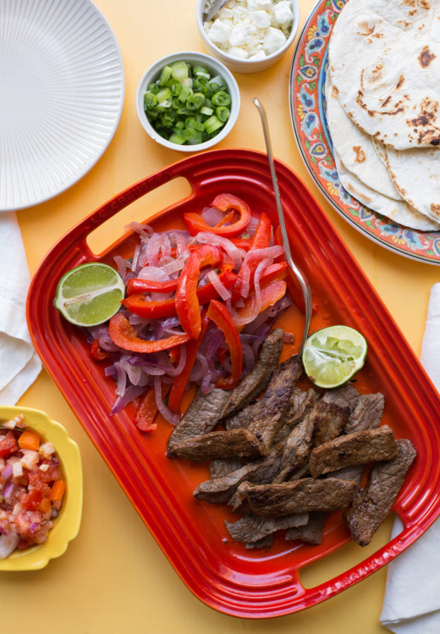 Red tray of Steak Fajitas, peppers, onions, and limes.