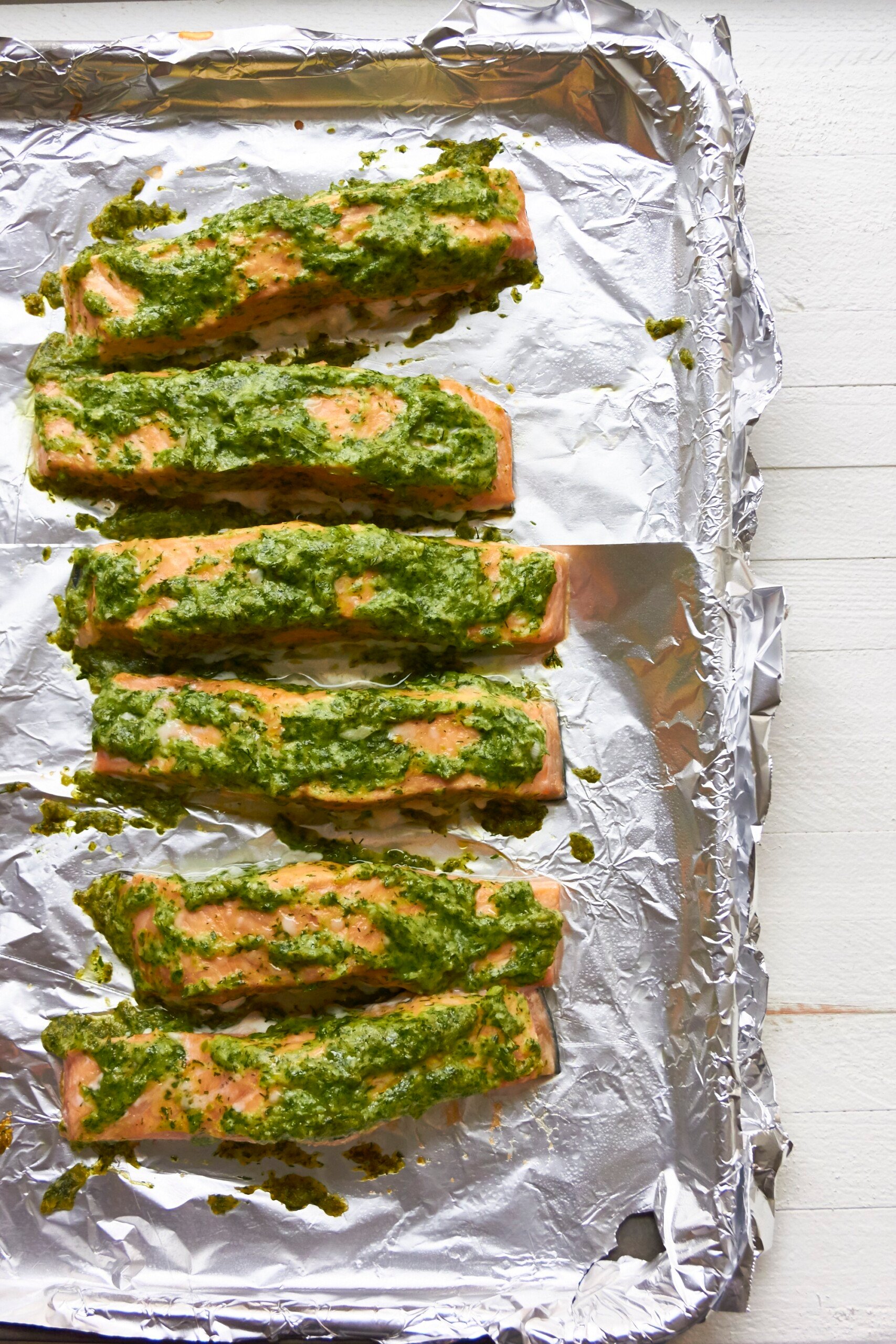 Several Herbed Salmon fillets on a baking sheet lined with foil.