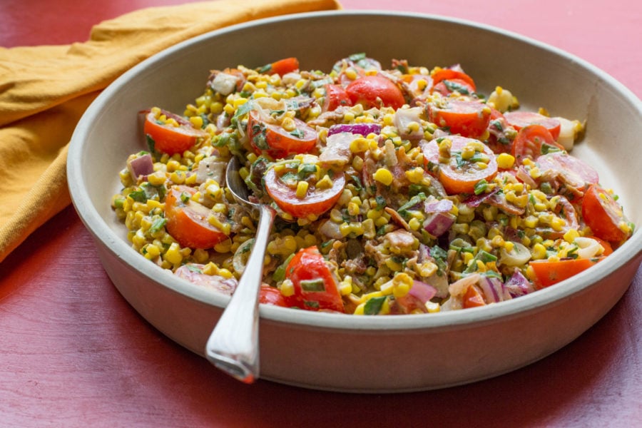 Summer Corn, Tomato and Bacon Salad in a bowl with a spoon.