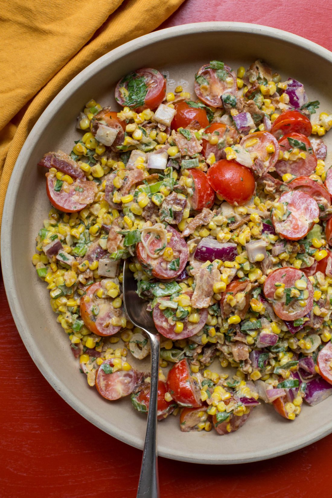 Spoon in a bowl of Summer Corn, Tomato and Bacon Salad.