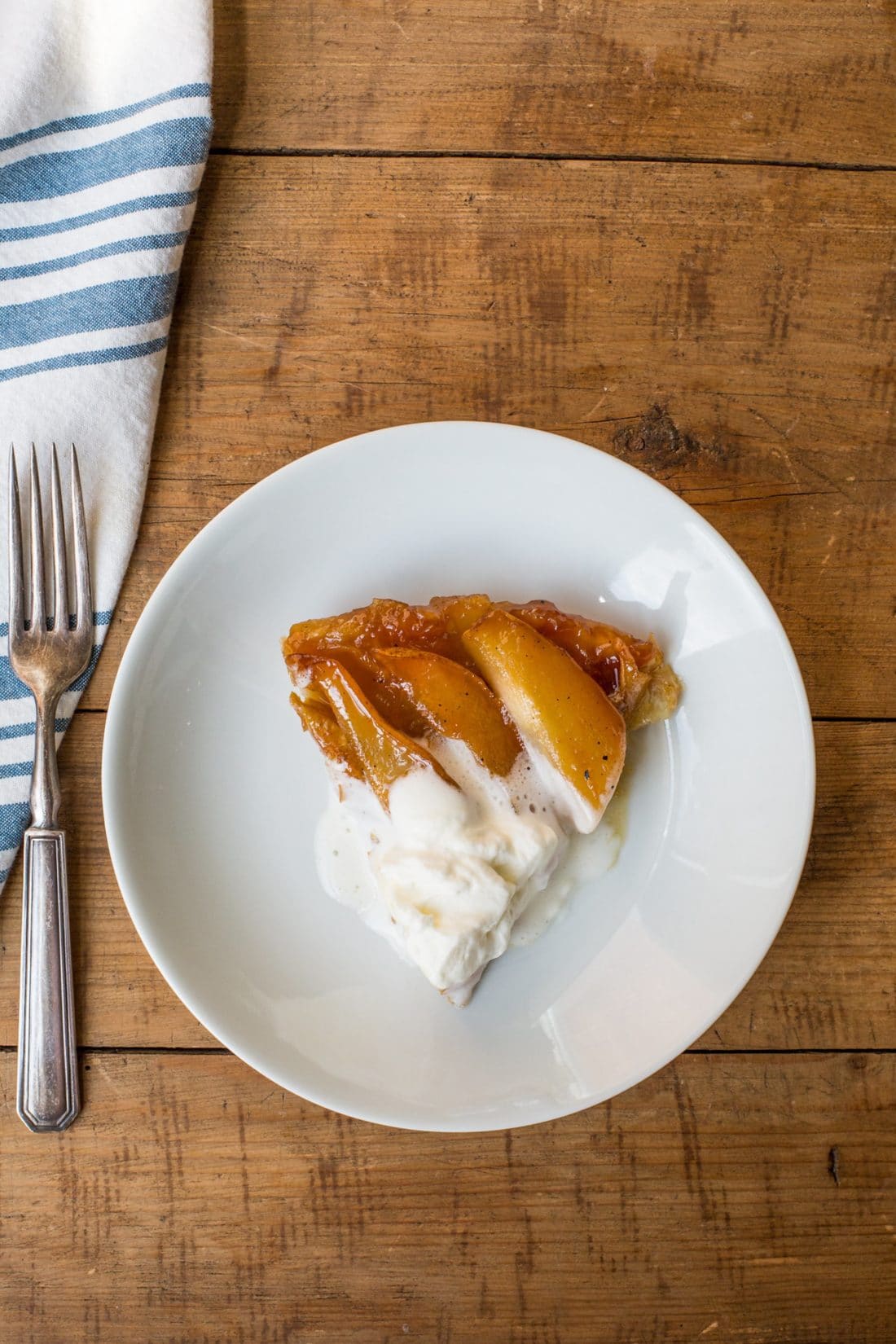 Plate with a slice of Pear Tart Tatin topped with sweetened whipped cream.