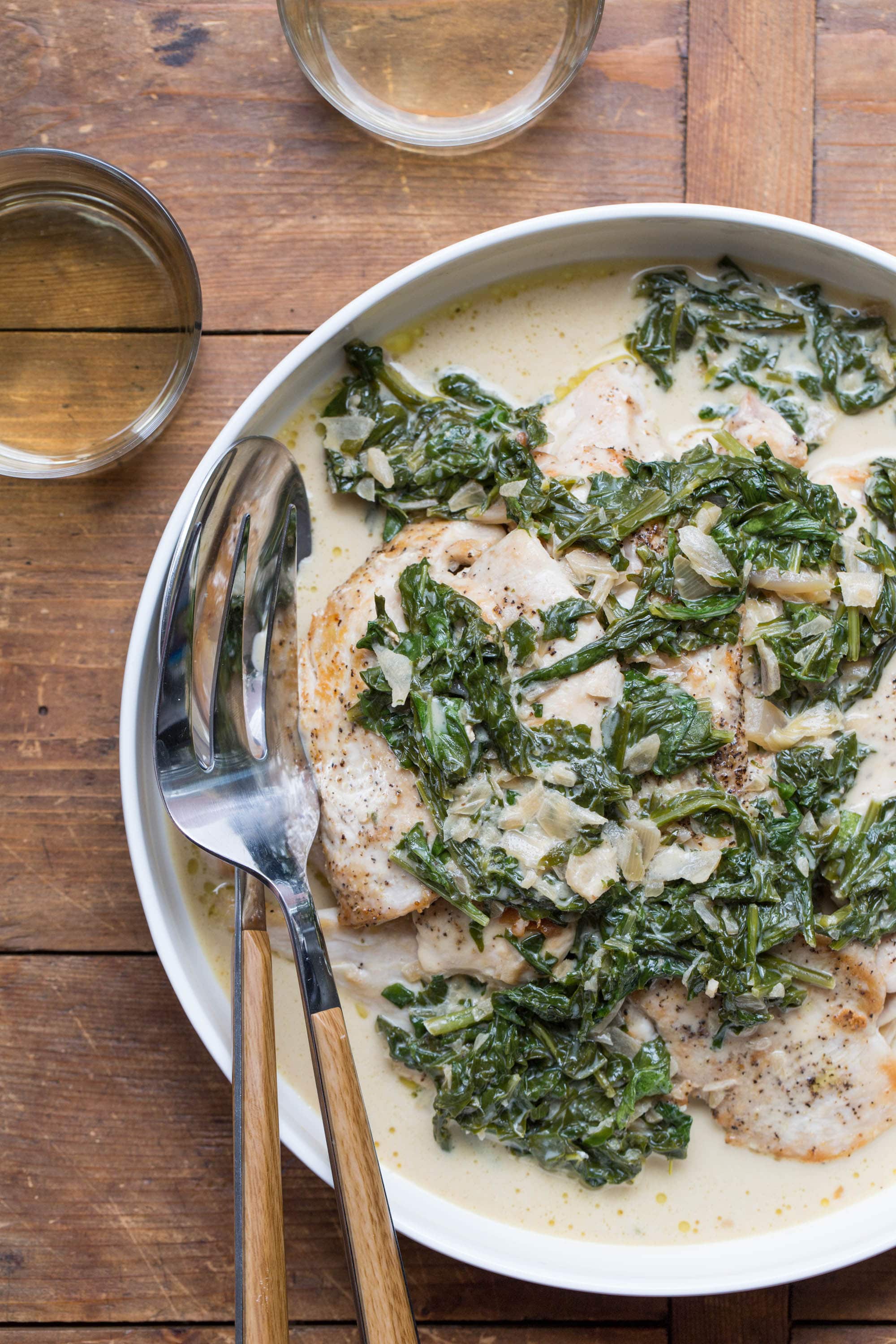 Chicken with Arugula and Mustard Pan Sauce in a white bowl with serving utensils.