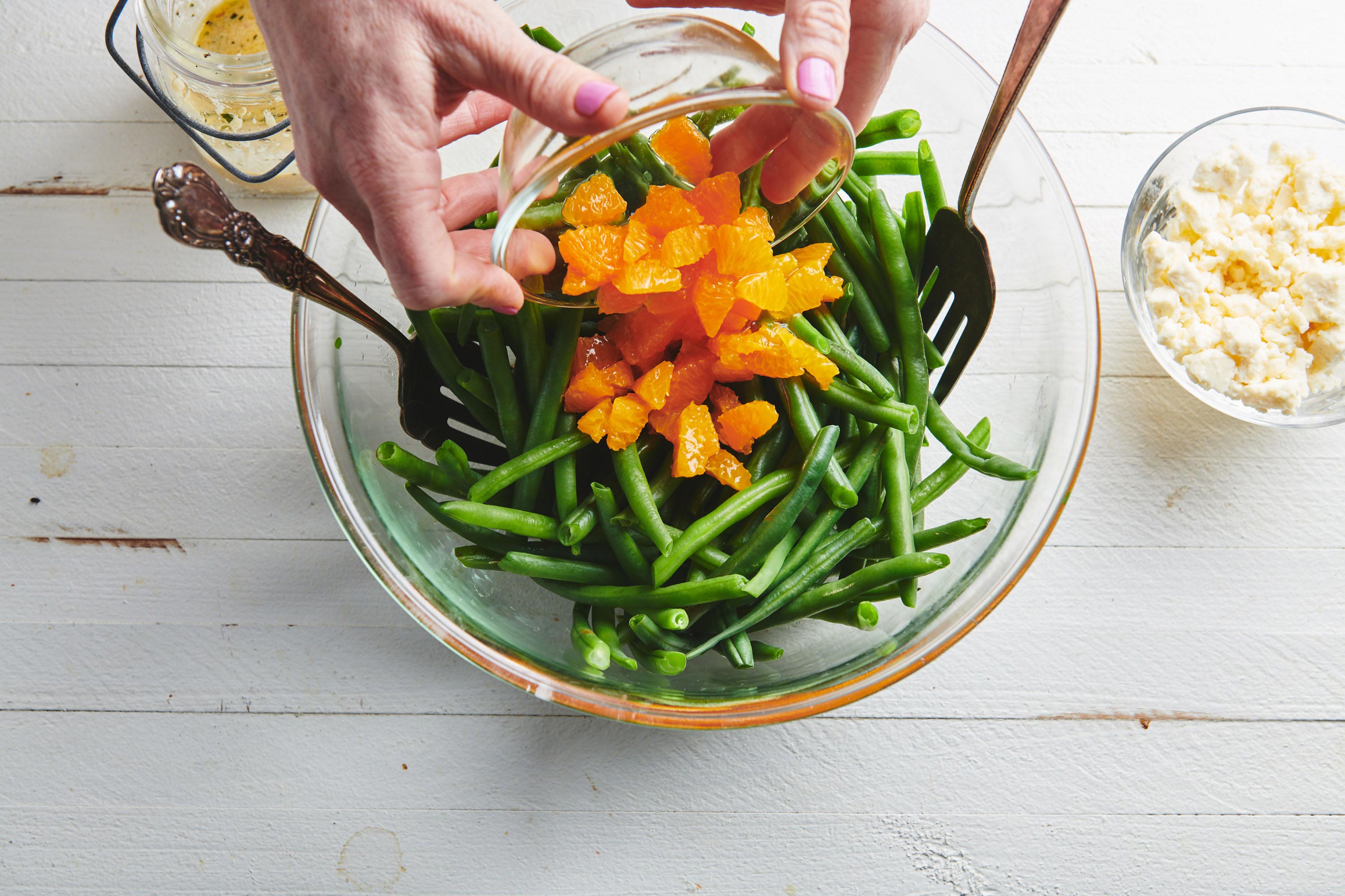 Woman pouring Clementine Oranges into a bowl of green beans.