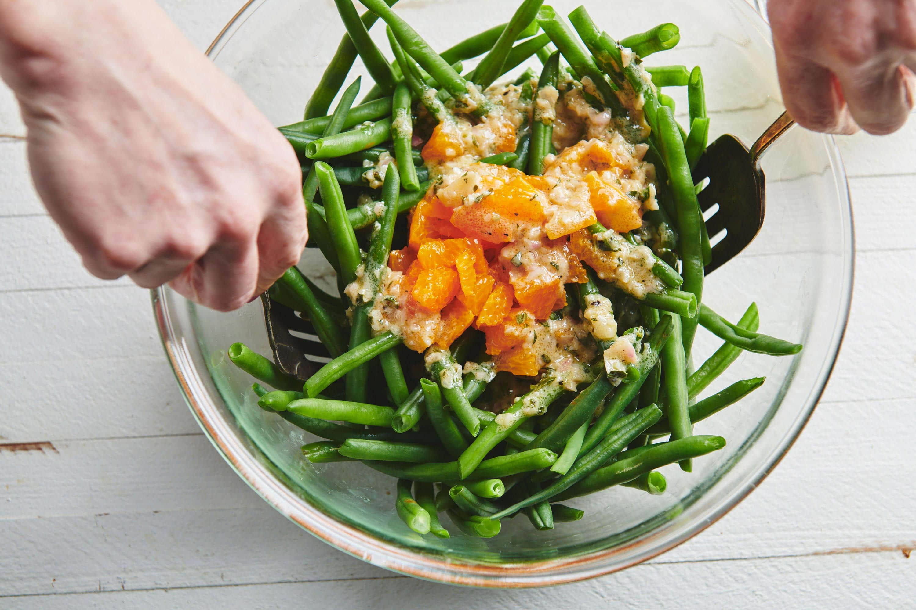 Woman tossing a bowl of green beans, clementine oranges, and dressing.