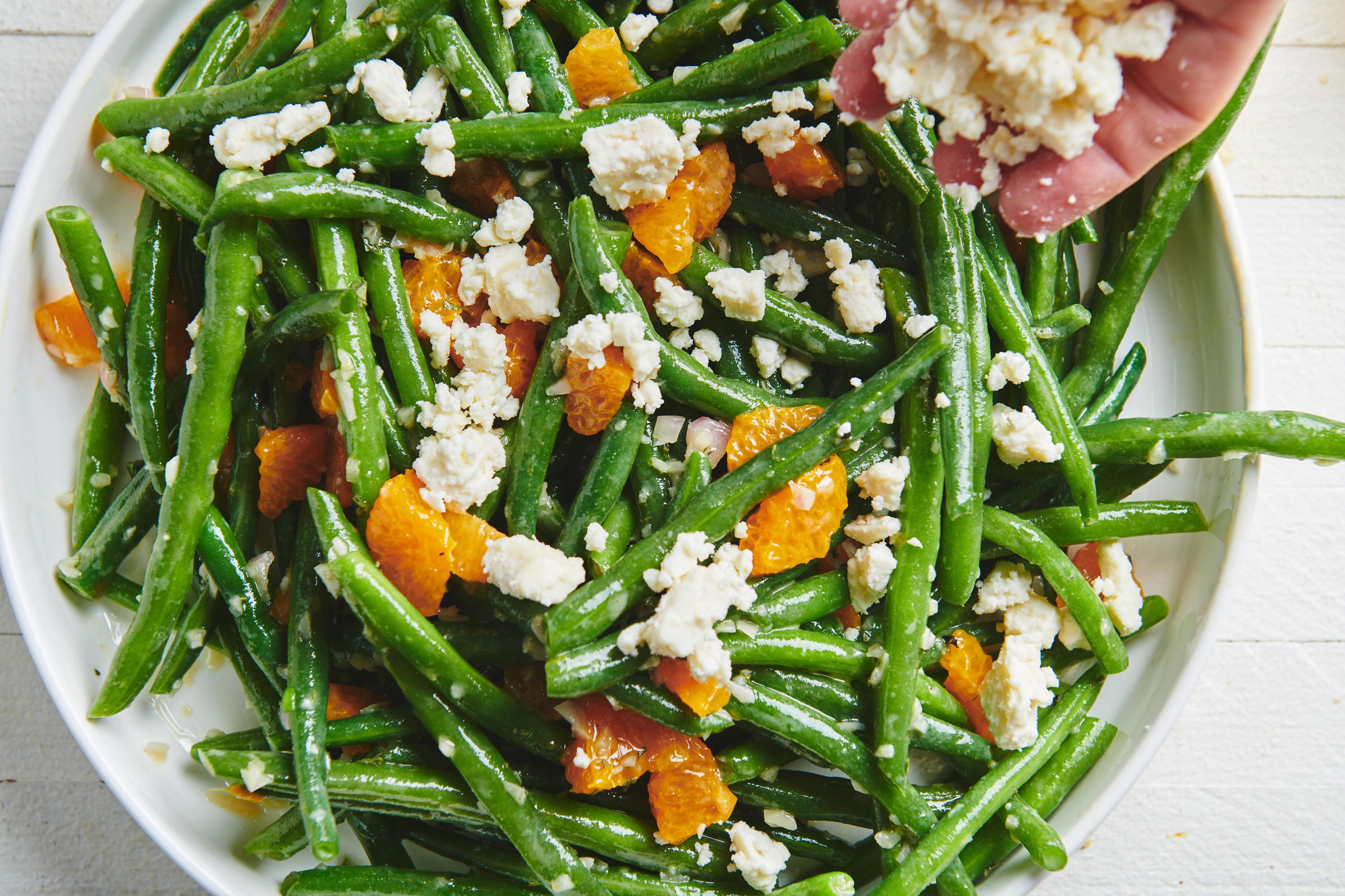Woman adding feta crumbles to a Green Bean Salad with Clementines.