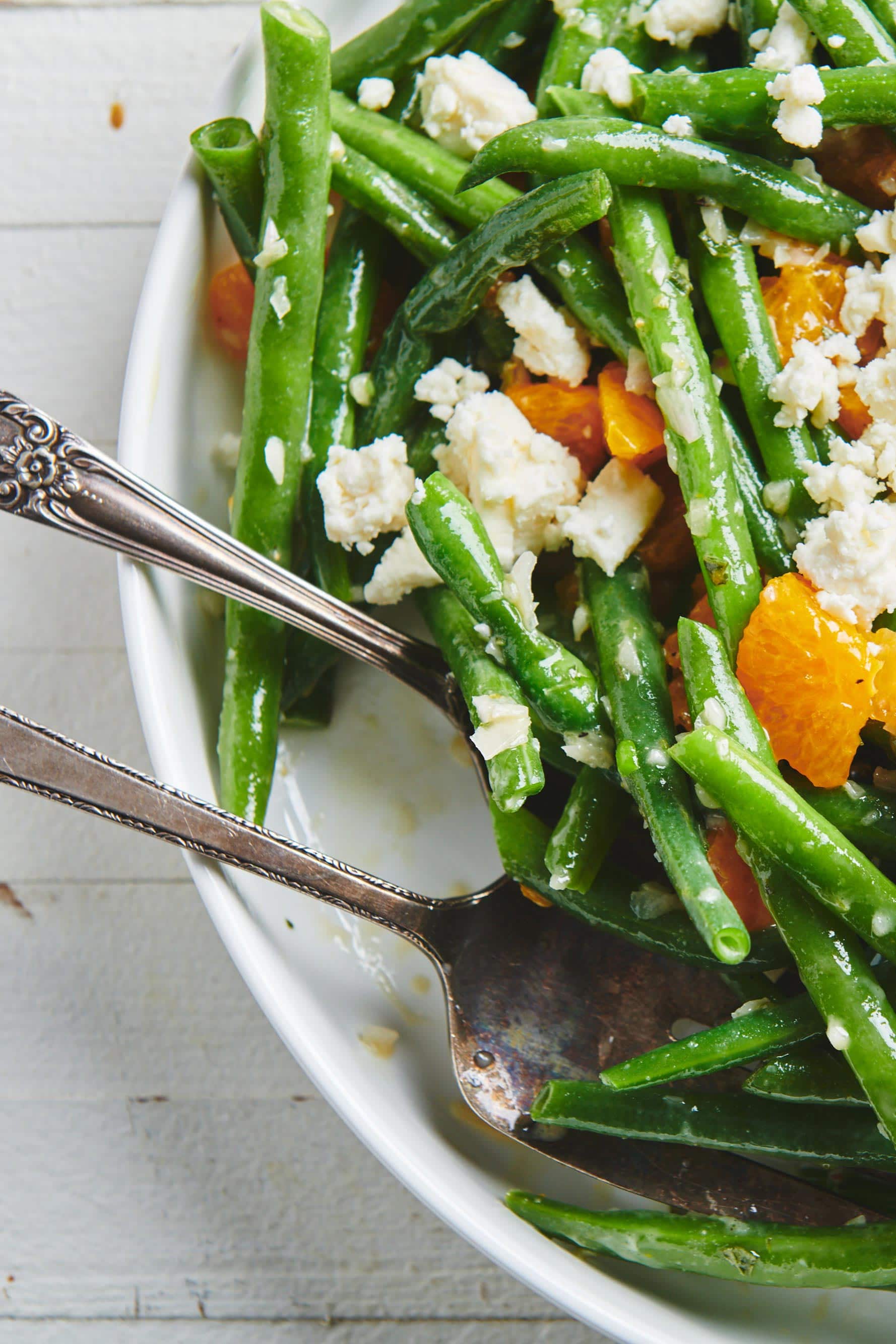Utensils in a serving dish of Green Bean Salad with Clementine Oranges and Feta.