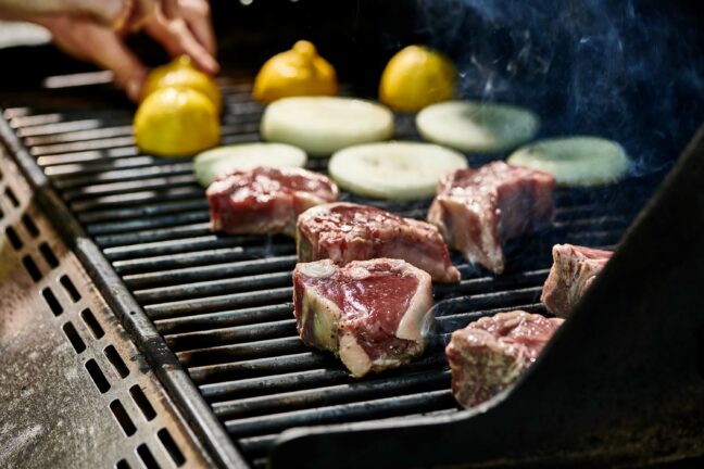 Lamb Chops, onion slices, and halved-lemons on a grill.