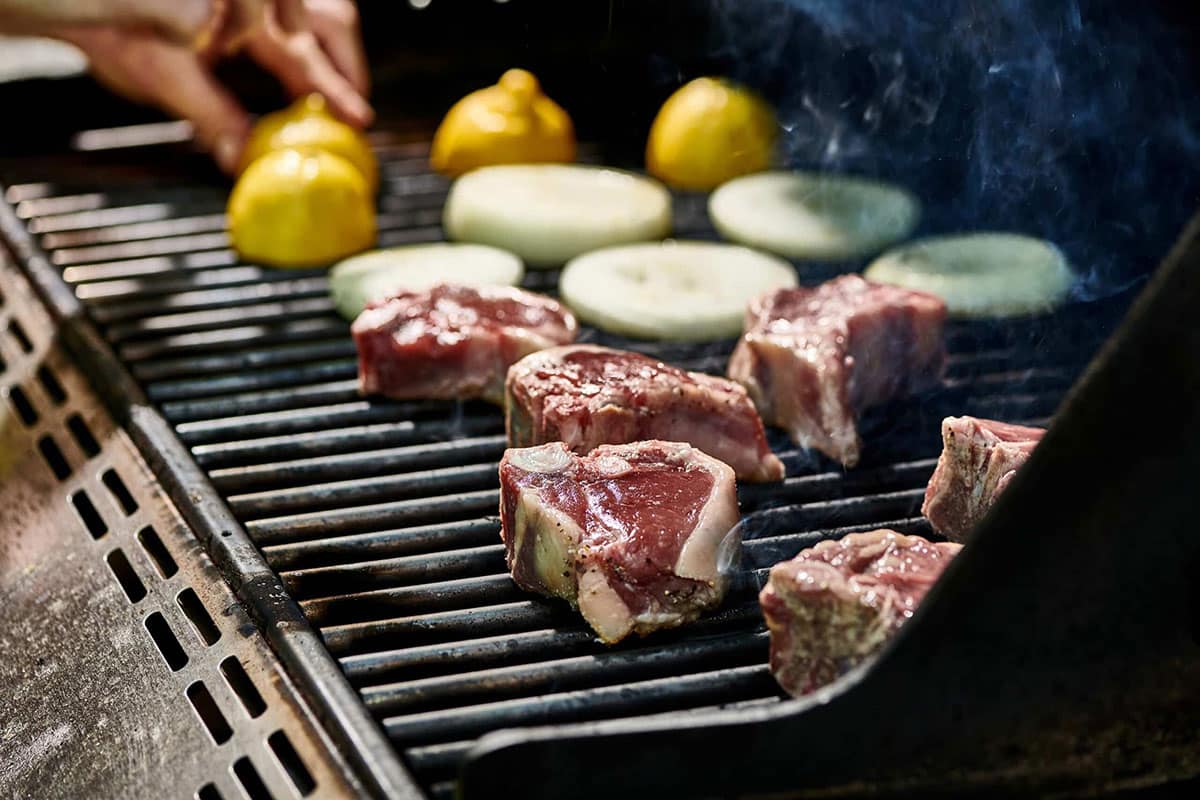 Lamb Chops, onion slices, and halved-lemons on a grill.