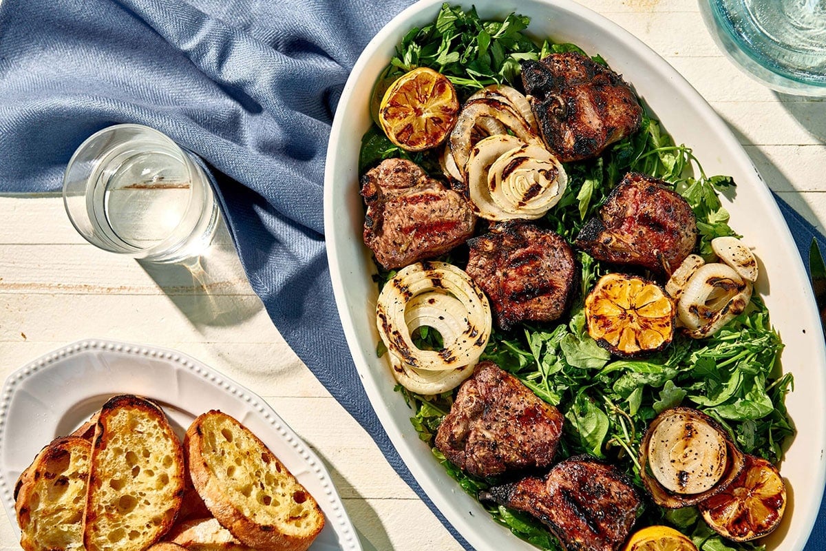 Grilled Lamb Chops and Onions with Herb Salad in a white dish.