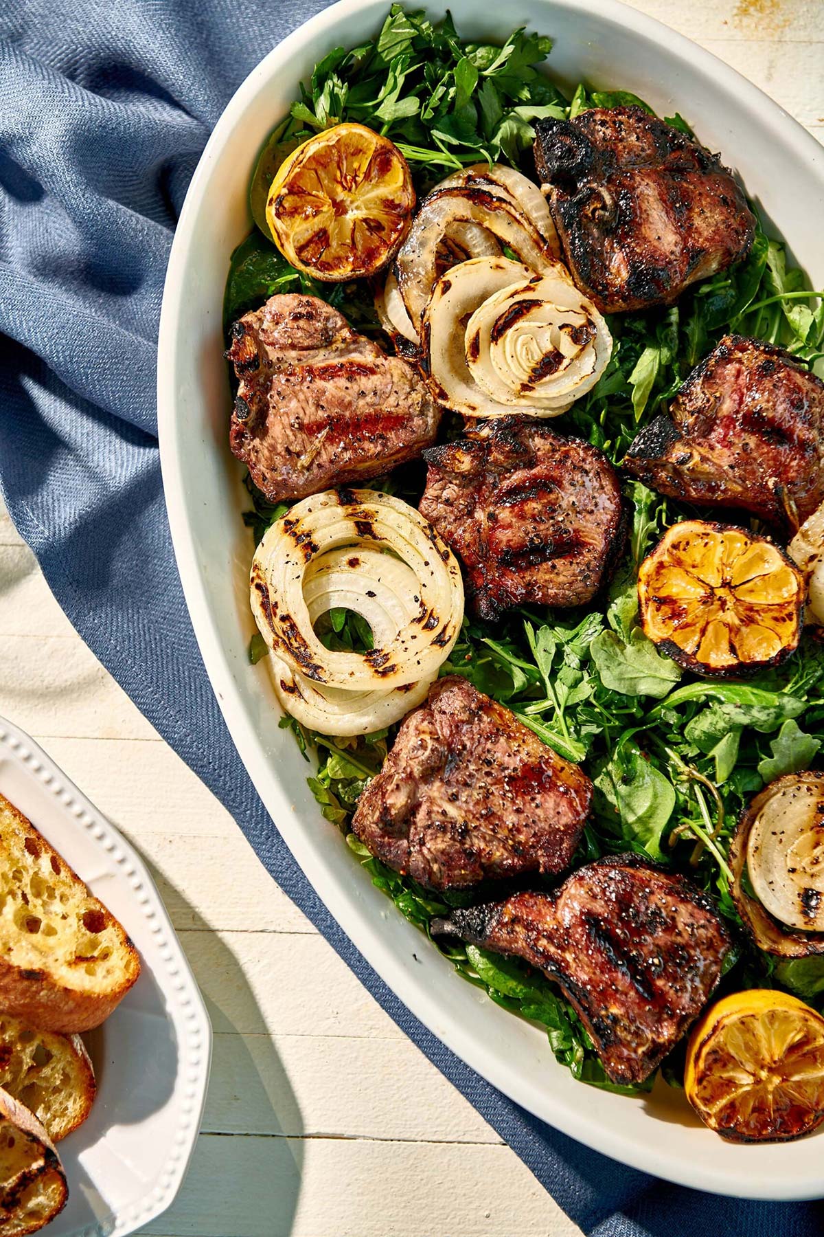 Oblong dish of Grilled Lamb Chops and Onions with Herb Salad.