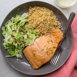 Hoisin glazed salmon with quinoa and salad on a gray plate next to pink napkin.