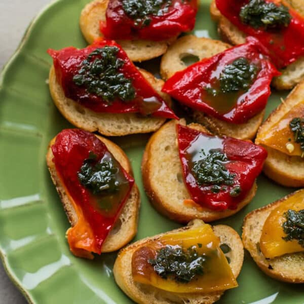 Crostini with roasted pepper and basil oil on green plate.