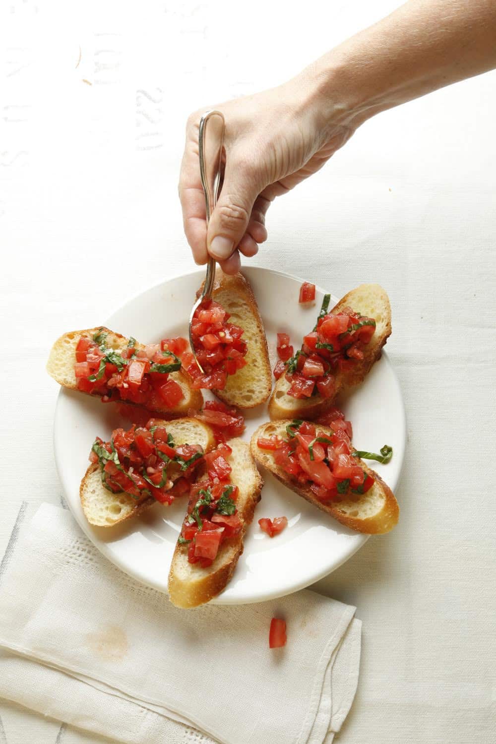 Woman spooning tomatoes onto bruschetta.