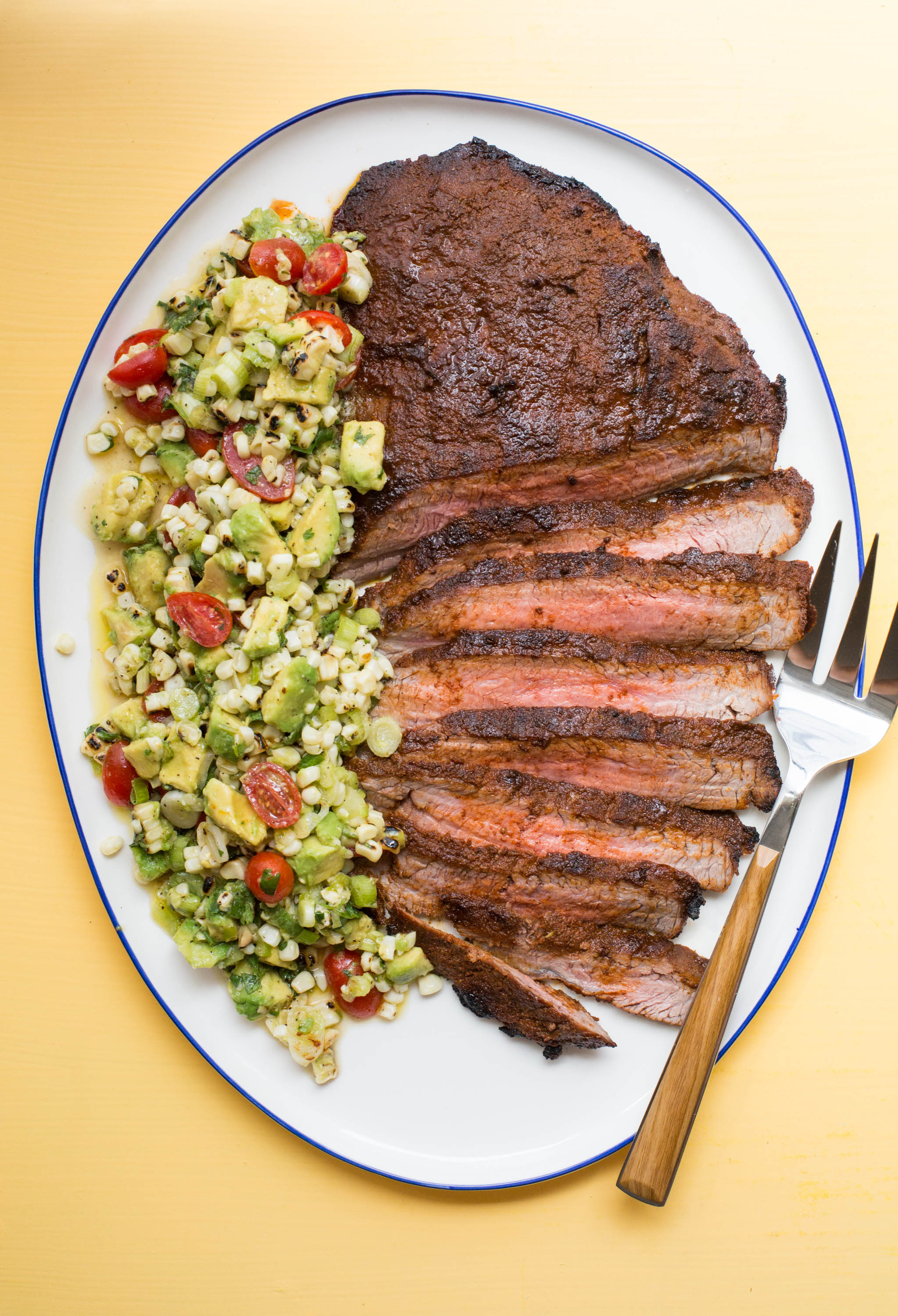 Fork on a plate of Chili Rubbed Flank Steak with Corn, Tomato and Avocado Salad.