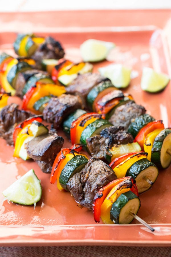 Beef Teriyaki Kebabs with Peppers and Zucchini on a tray with cut limes.