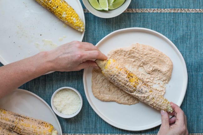 Rolling grilled corn in mayo mixture