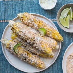 Mexican Grilled Corn on white plate with lime wedges.
