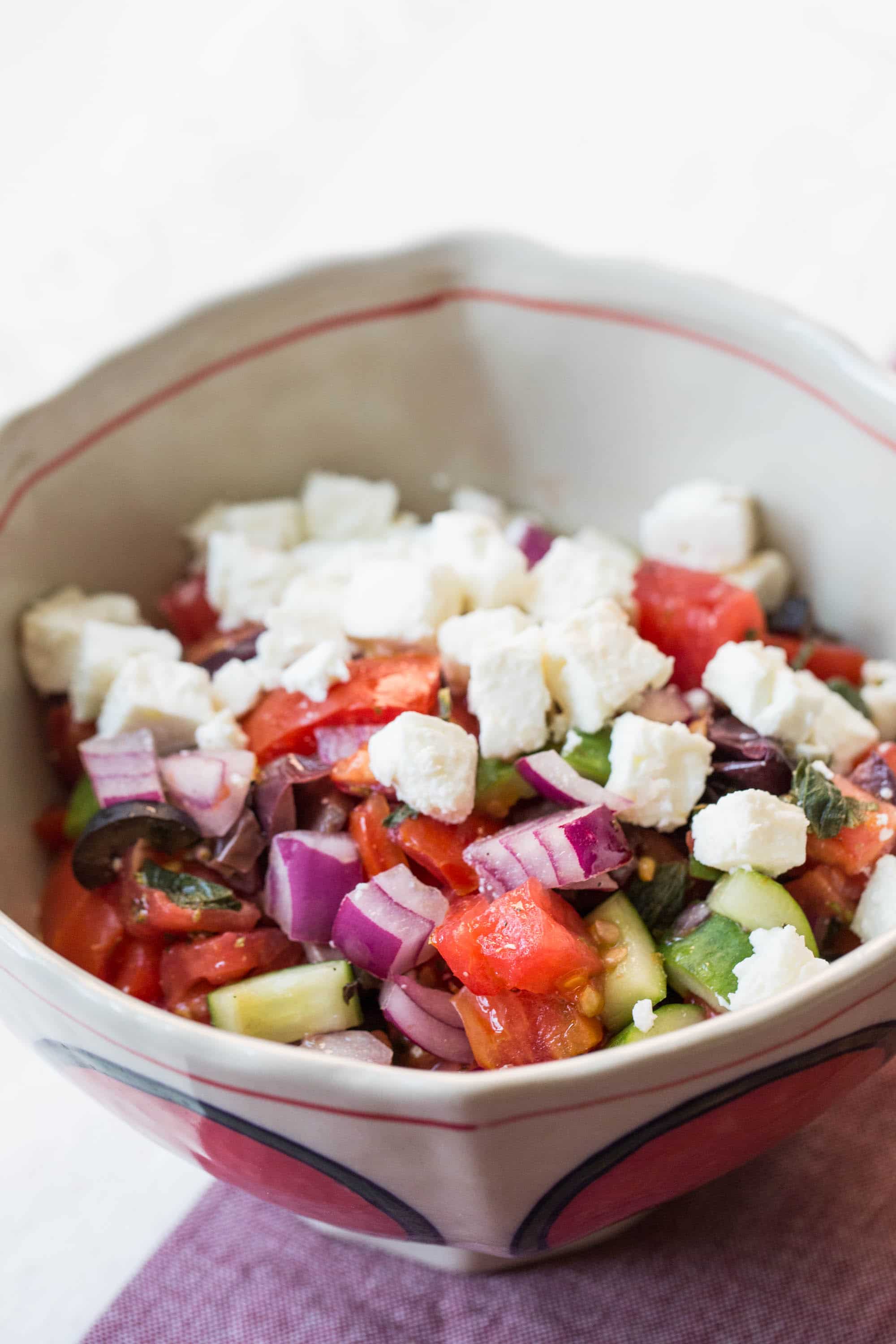 Tan bowl with Greek Tomato and Cucumber Salad topped with feta cheese.