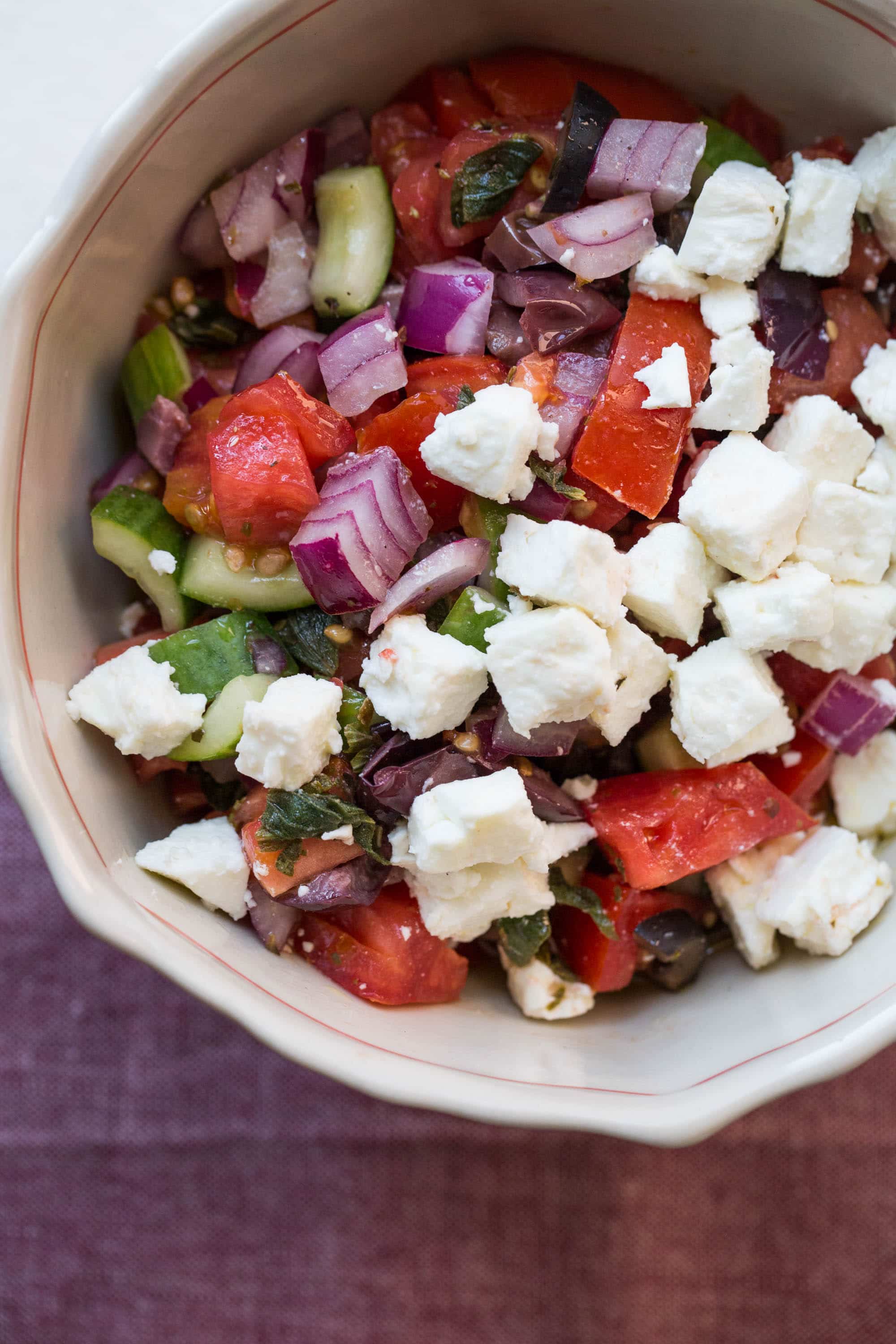 Greek Tomato and Cucumber Salad with feta crumbles in tan bowl.
