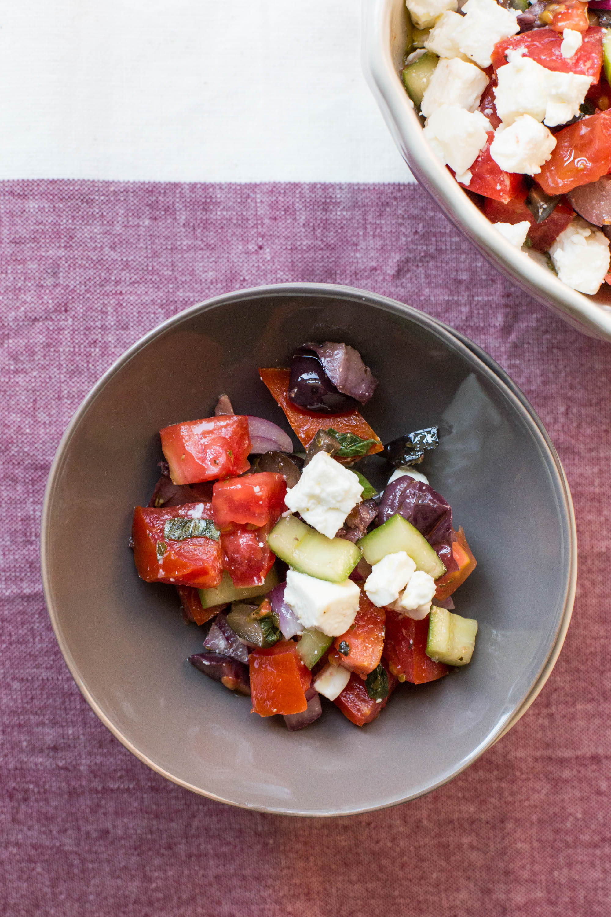 Greek Tomato and Cucumber Salad in bowl on burgundy tablecloth.