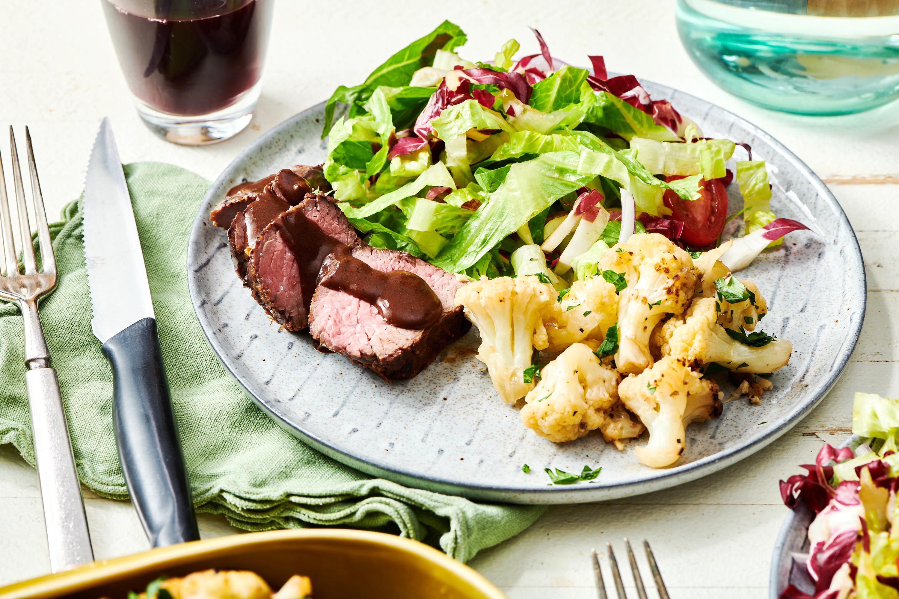 Plate of Braised Cauliflower, meat, and green salad.