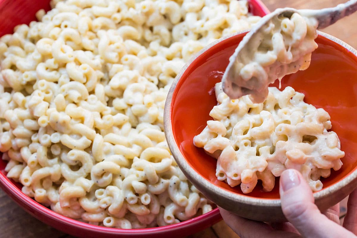 Scooping white mac and cheese into orange bowl.