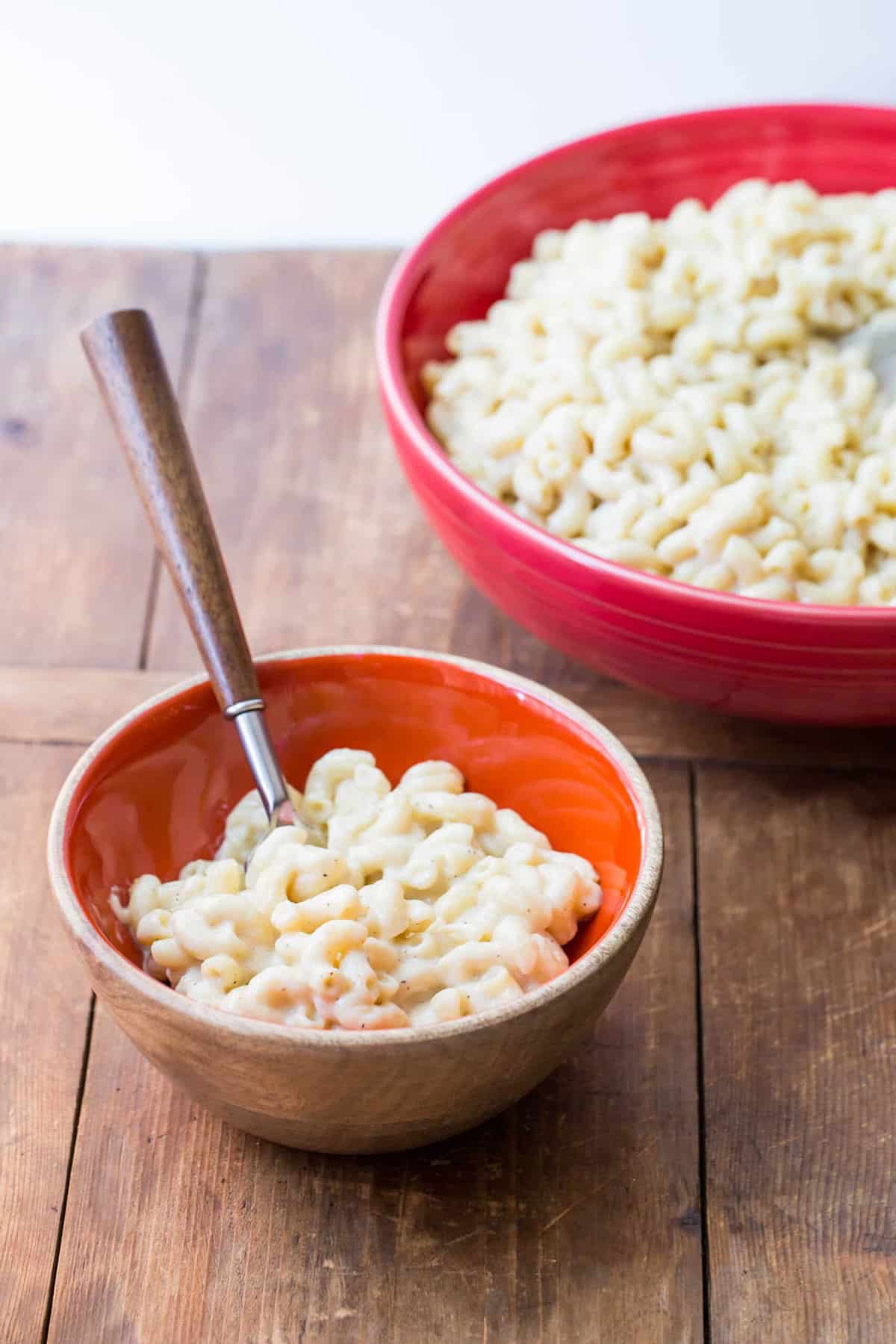 Homemade white mac and cheese in red and orange bowls on table.