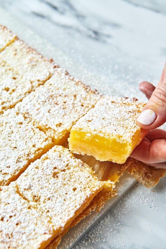 Woman grabbing a Lemon Square from parchment paper.