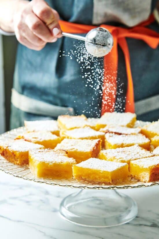 Woman sprinkling powdered sugar onto Lemon Squares.