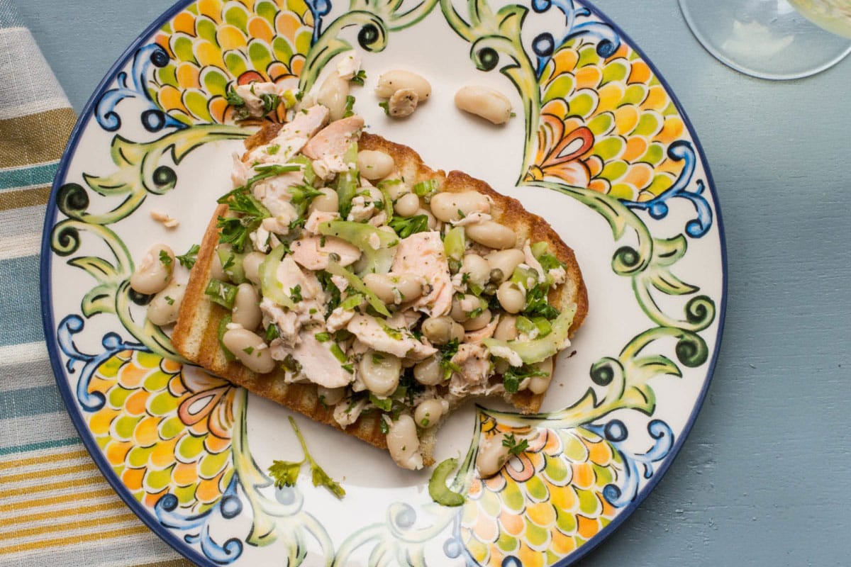 Colorful plate with a Salmon and White Bean Bruschetta missing a bite.