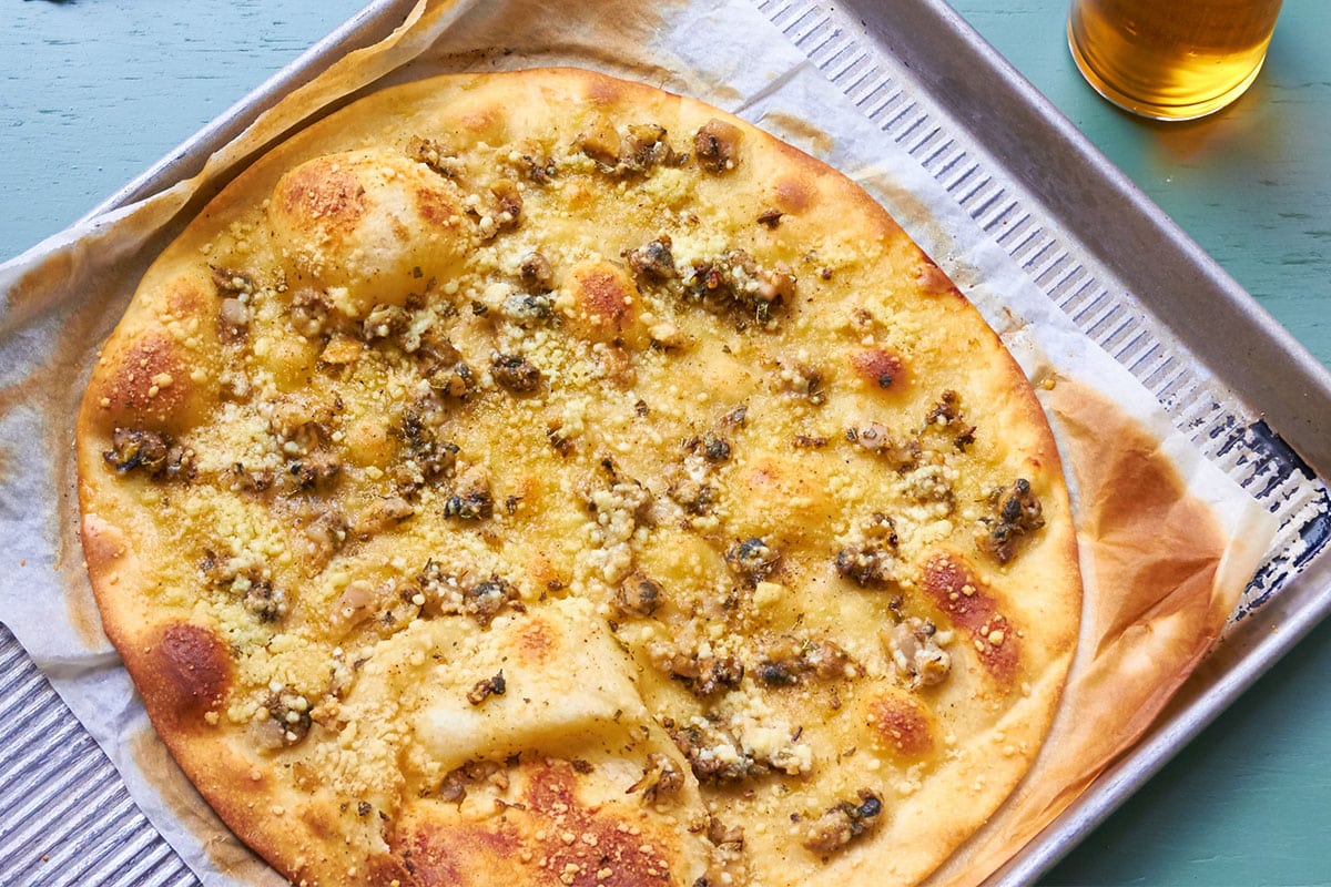 White clam pizza on baking sheet next to beer on table.