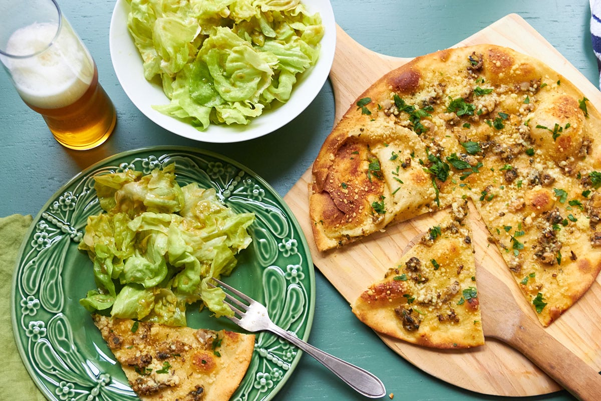 White clam pizza sliced on pizza board and plate with salad and beer.