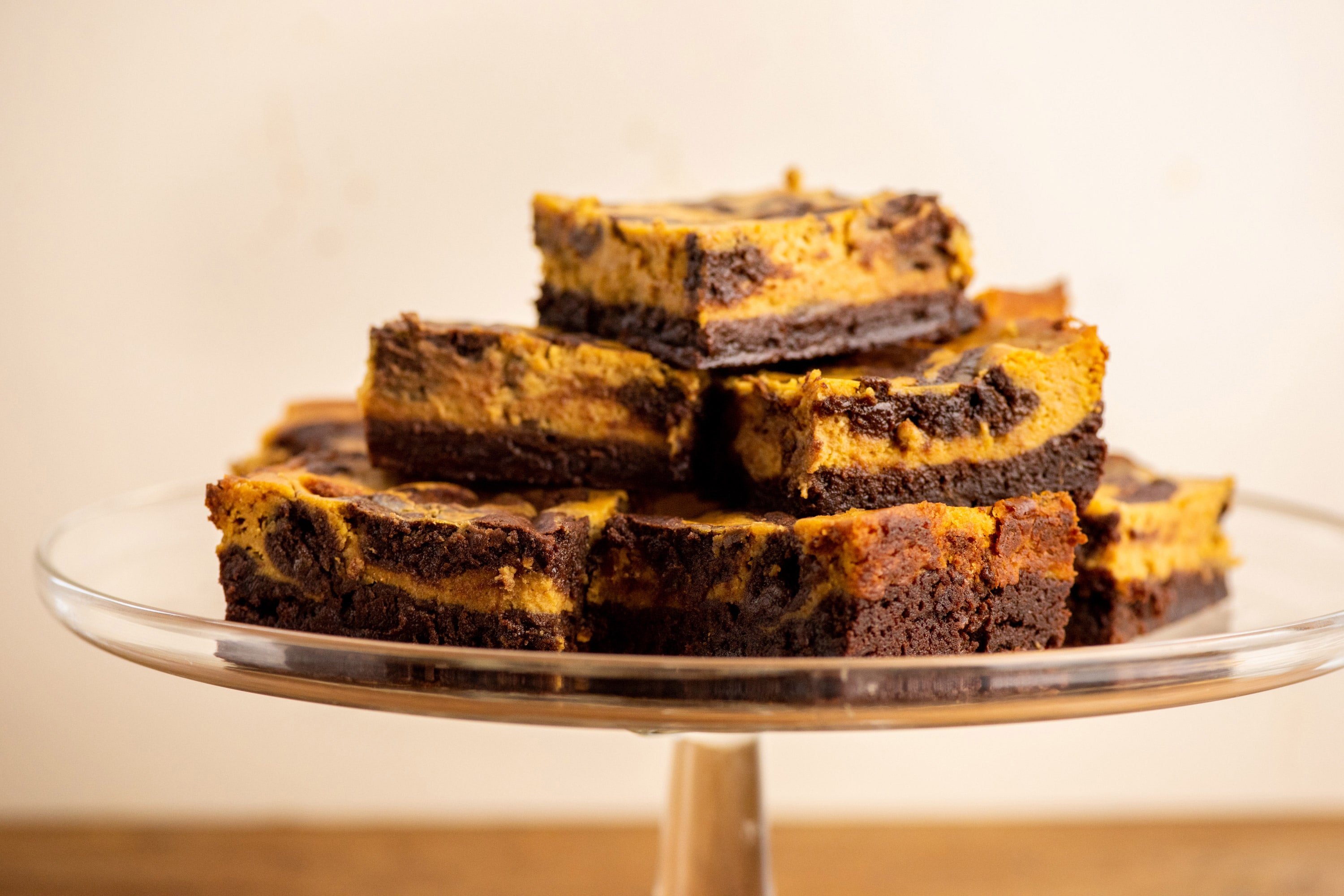 Pumpkin Cream Cheese Brownies stacked on a glass serving dish.