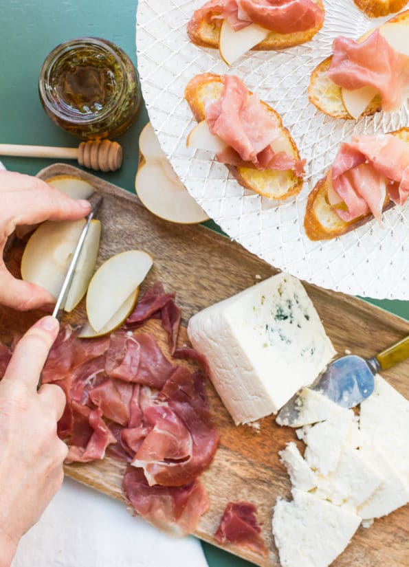 Person slicing an Asian pear on a wooden tray with Prosciutto and Blue Cheese.