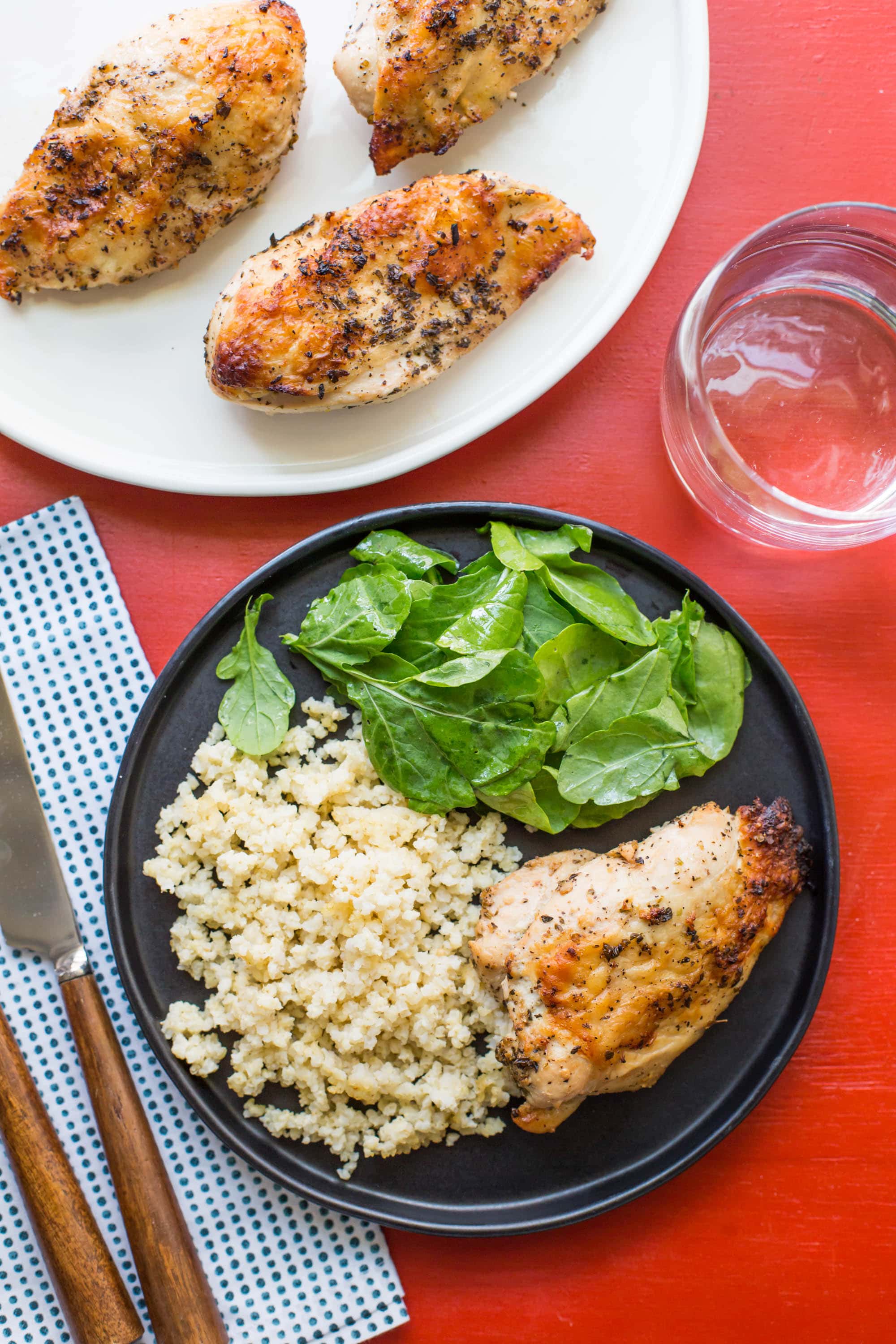 Greek Roasted Chicken Breasts on plates with salad and rice.