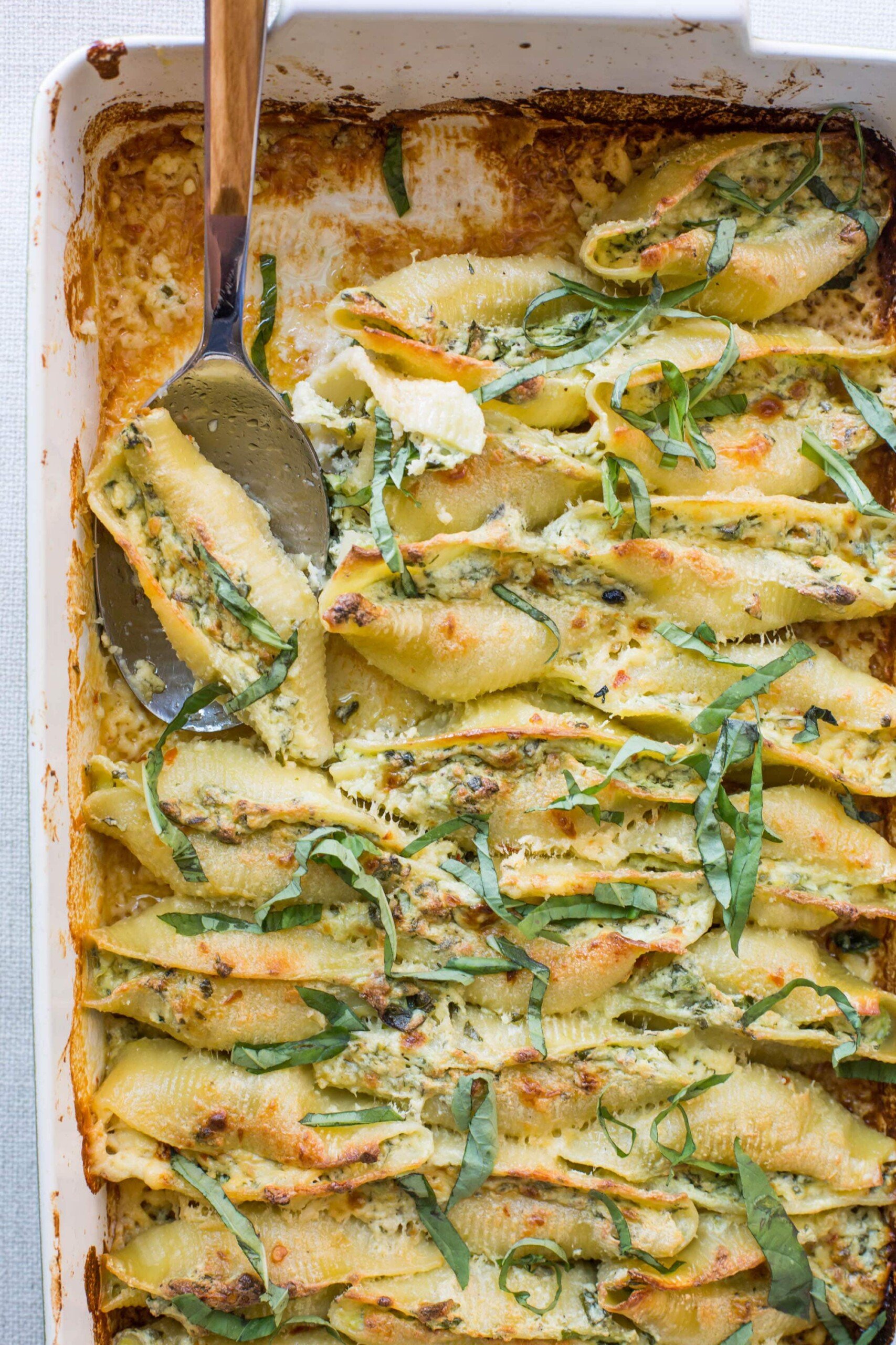 Fork scooping a Spinach and Cheese Stuffed Shell from a baking dish.