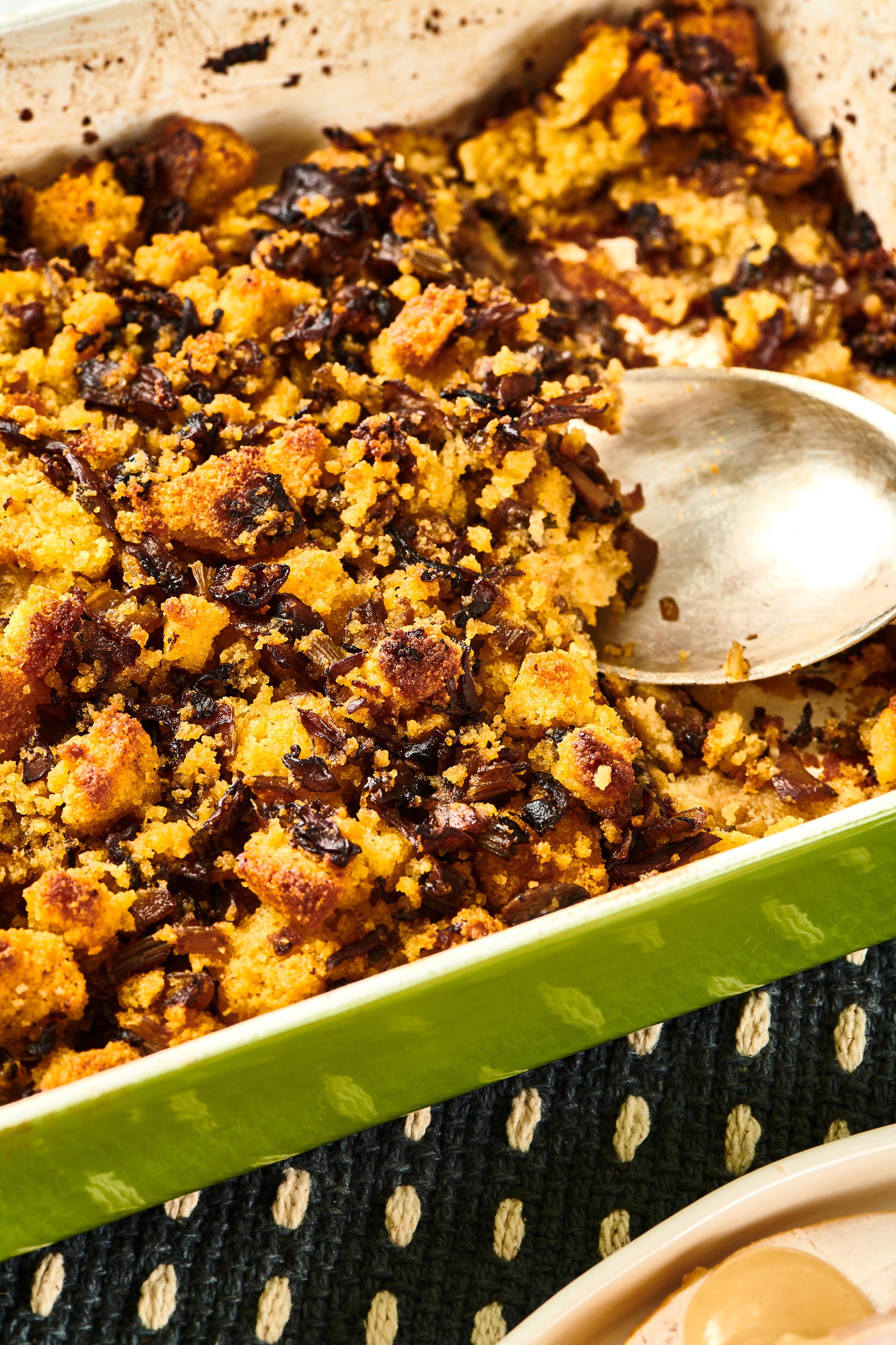 Spoon scooping Cornbread Dressing from a green baking pan.