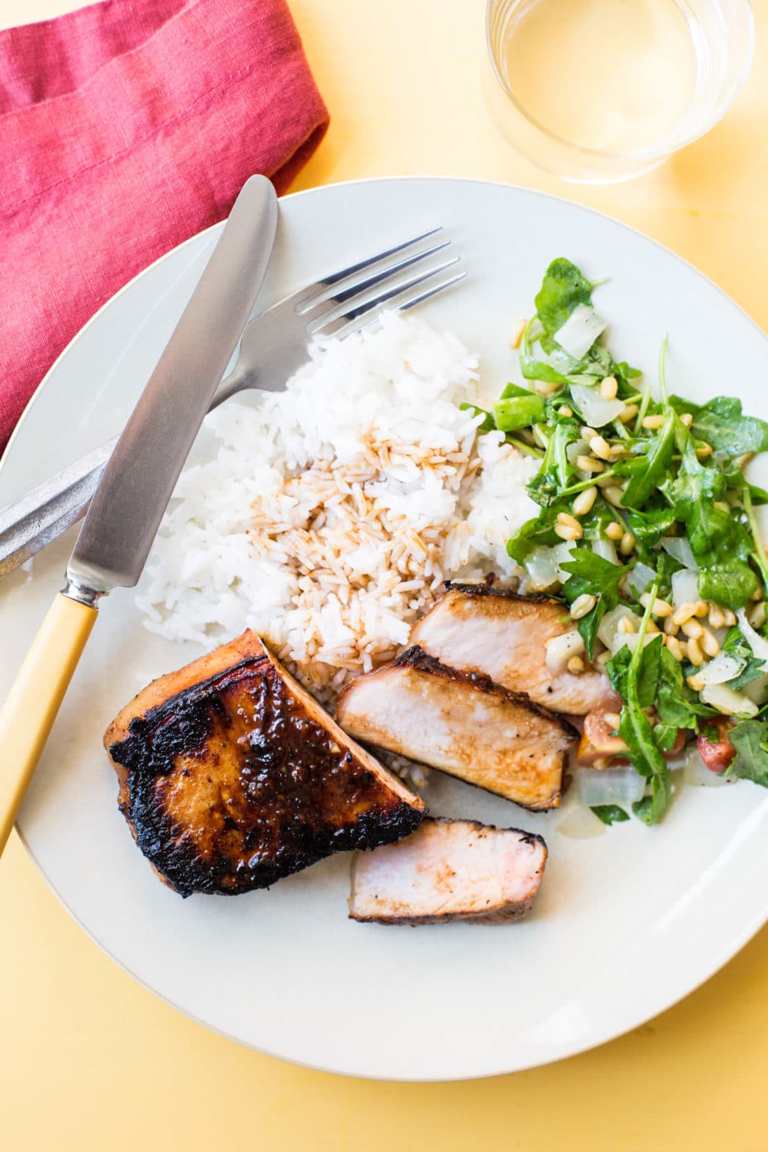 Rice, salad, and a Korean Pork Chop on a plate with silverware.