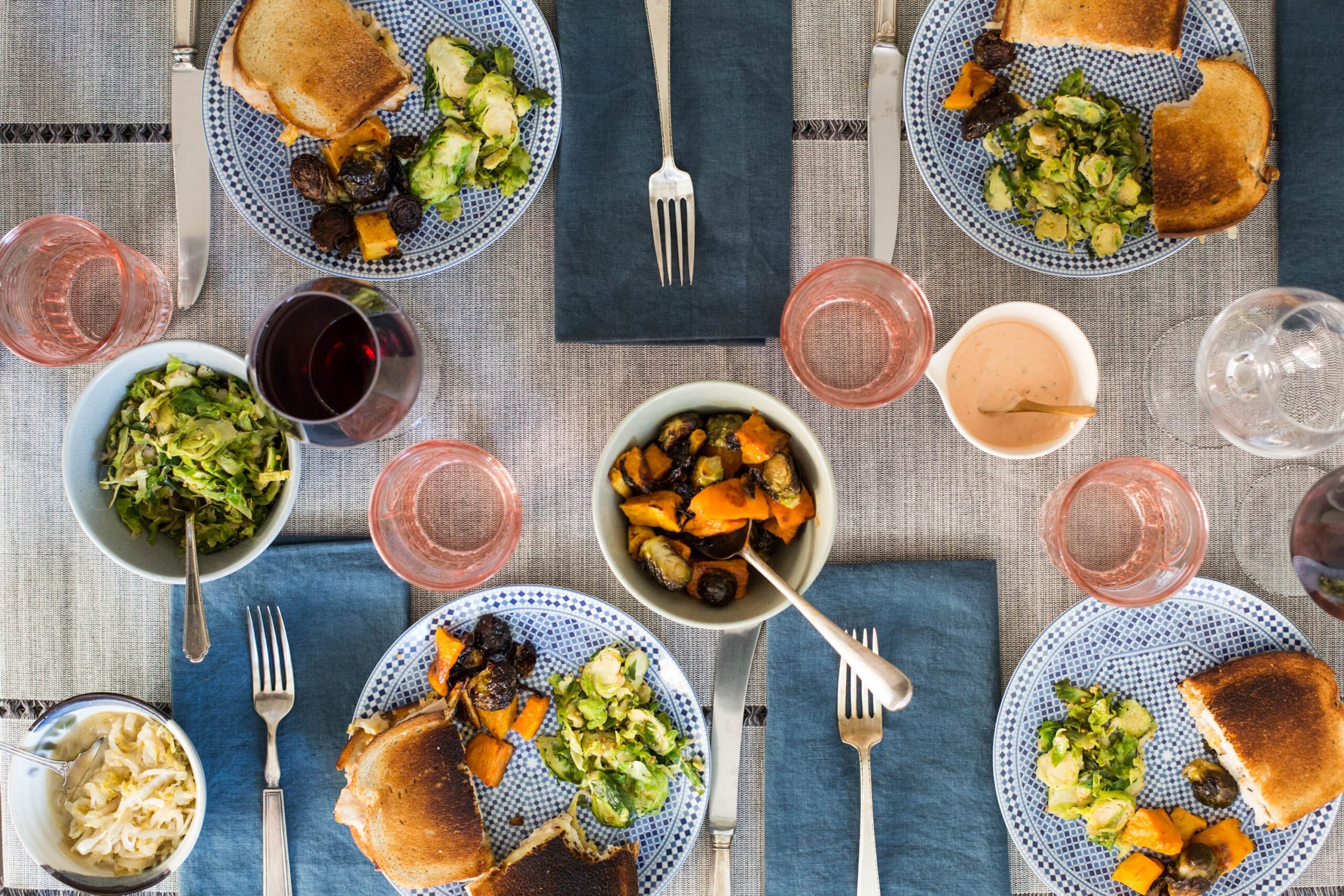 Plates of Turkey Reuben Sandwiches, brussels sprouts, and vegetables on table.