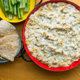 Red bowl of Spicy Cheesy Artichoke Dip.