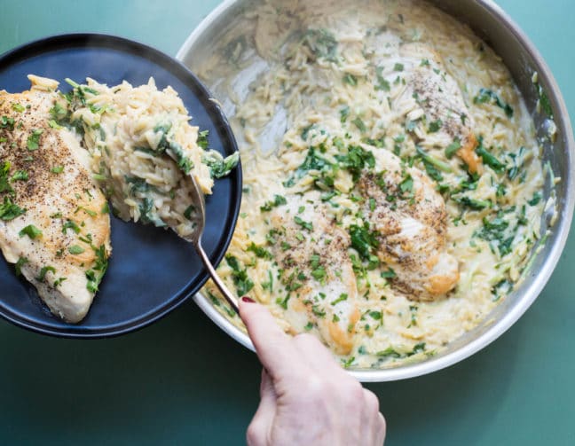 Woman serving Cheesy Chicken and Orzo onto a blue plate.