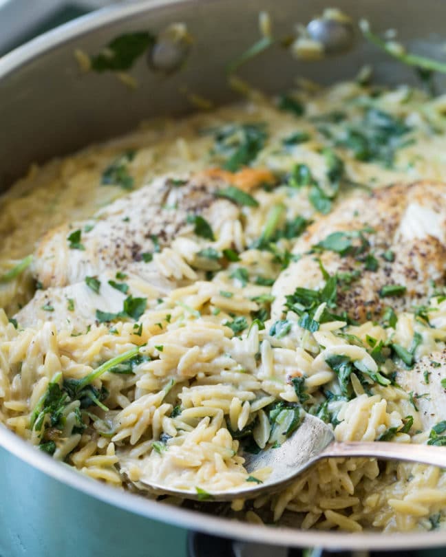 Spoon in a skillet of Cheesy Chicken and Orzo.