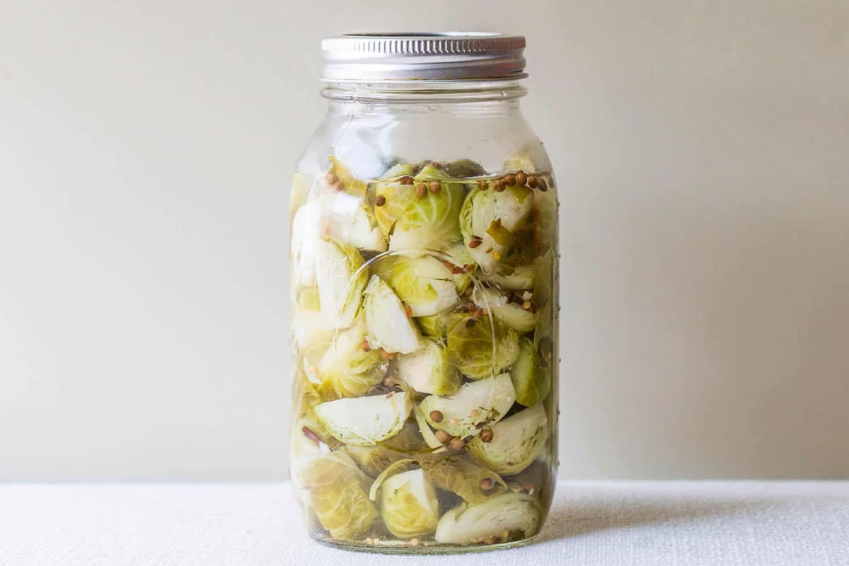 Pickled Brussels sprouts in Mason jar on table.