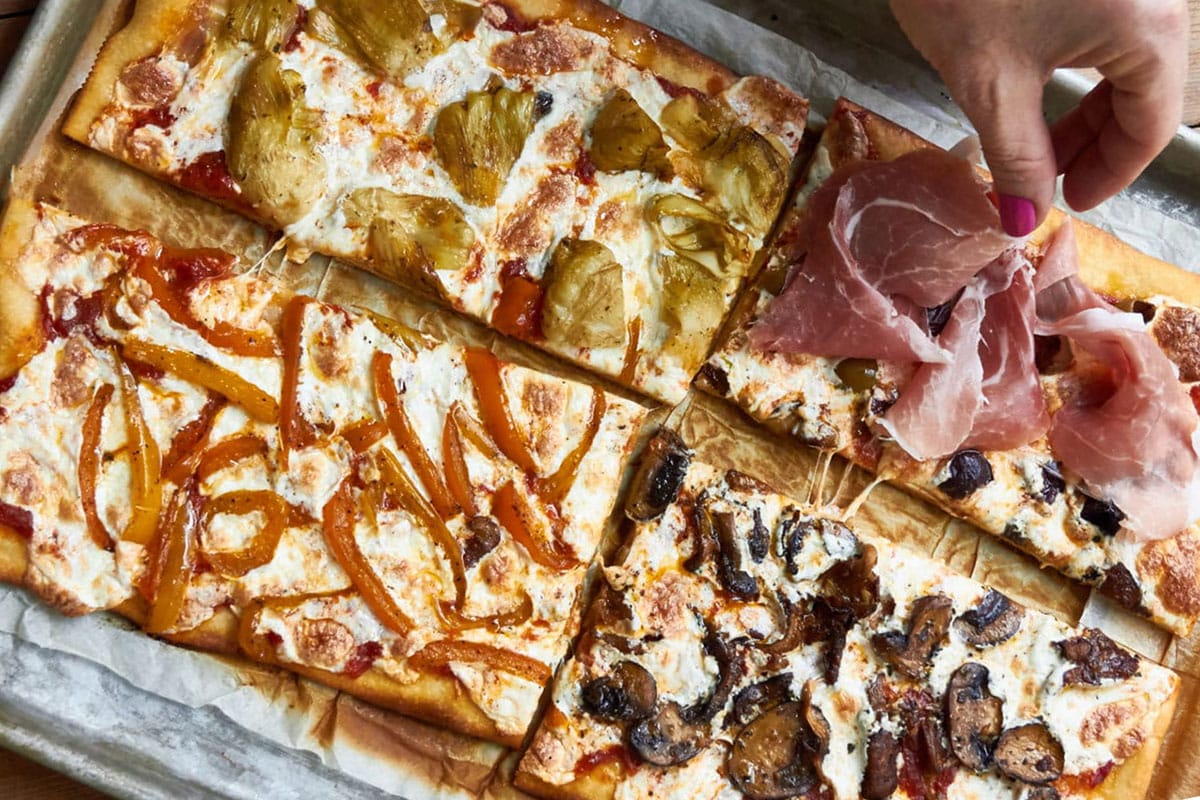 Woman draping prosciutto over one quarter of a Pizza Quattro Stagioni.