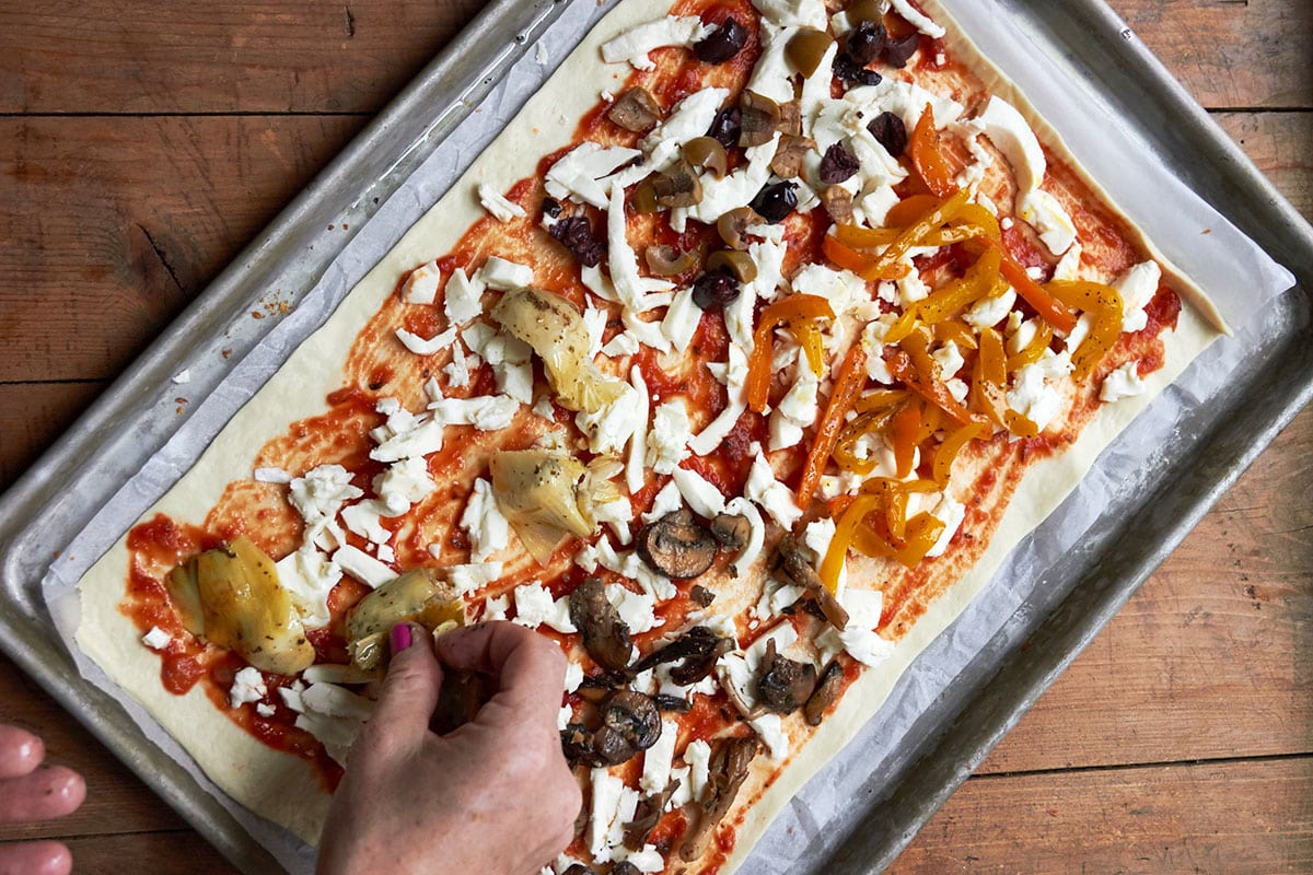 Placing mushrooms, onions, tomatoes, and other toppings on four season pizza.