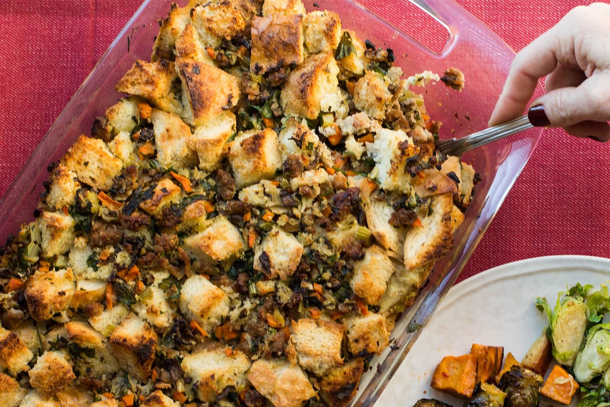Serving turkey sausage stuffing from baking dish with spoon.